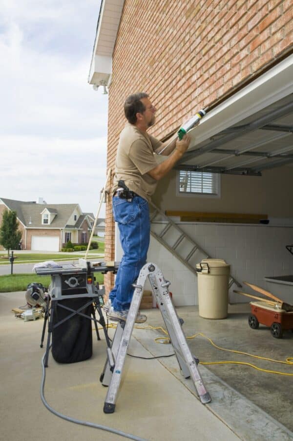 Carpenter caulking cracks between garage door frame and brick